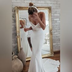 a woman standing in front of a mirror wearing a white dress and holding her hand to her face