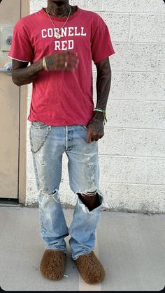 a man standing in front of a door wearing ripped jeans and a red shirt