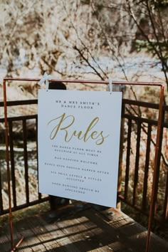 a sign that is on the side of a wooden bridge with trees in the background