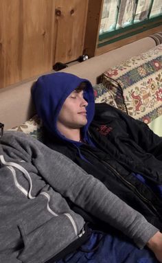 a man laying on top of a bed wearing a blue hoodie and looking off into the distance