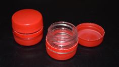 three red plastic containers with lids on a black surface, one is empty and the other two are closed