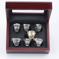 six silver and gold rings in a wooden display case on a white surface with a black background