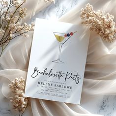 a white card with a martini glass on it next to some dried flowers and leaves