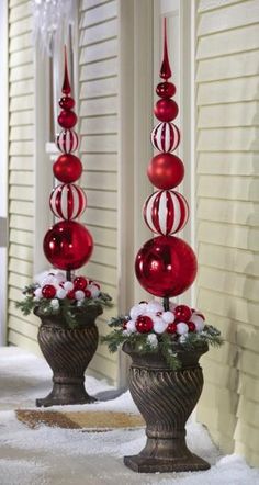 two red and white christmas ornaments in urns on snow covered ground next to house