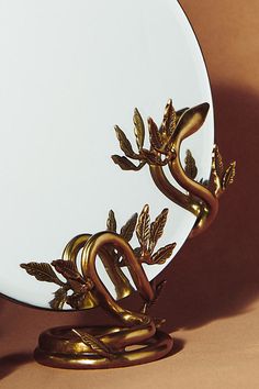 a mirror with a gold snake on it's face and leaves in the reflection