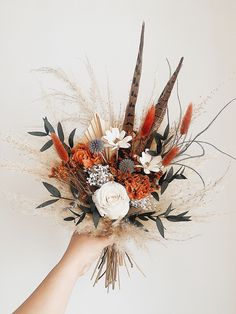 a hand holding a bouquet with feathers and flowers in it's centerpiece, against a white background