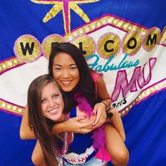 two girls hugging each other in front of a welcome sign