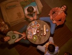 three people sitting at a table with plates and drinks in front of them, looking down