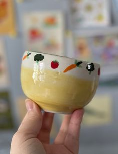 a person holding up a small bowl with fruit on the inside and vegetables painted on it