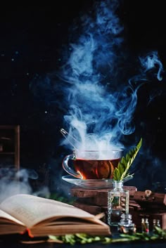 a cup of tea with steam rising out of it next to an open book