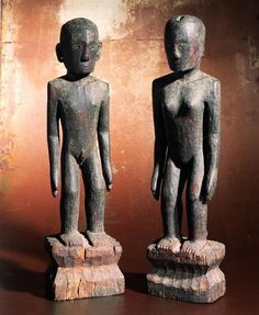 two wooden statues sitting next to each other on top of a brown surface with rusted paint