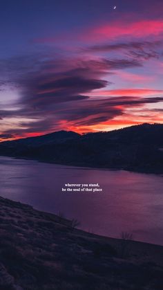 the sky is pink and purple as it sits over water with mountains in the background