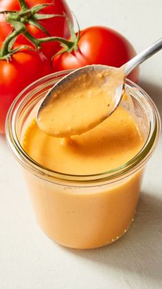 a spoon full of dressing with tomatoes in the back ground and on top of it