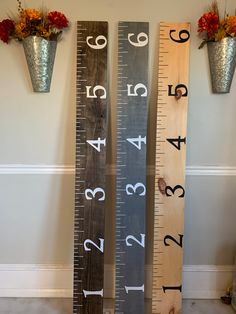 two tall wooden rulers with numbers on them next to flower vases and potted plants