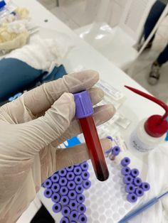 a gloved hand holding a purple tube with red liquid in it on top of a table