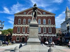 a statue in front of a building with people sitting on benches and walking around it