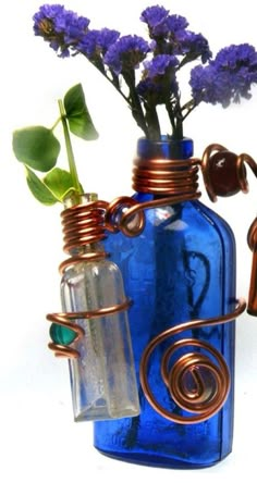 a blue glass vase with flowers in it and some copper wire wrapped around the bottle