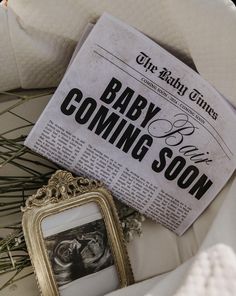 a baby coming soon newspaper sitting on top of a white chair next to a framed photo