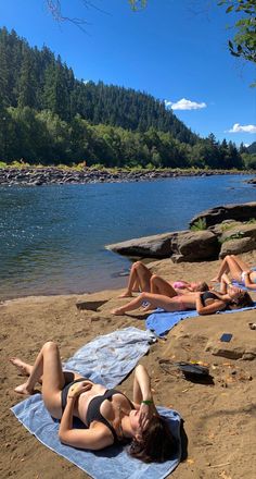 two women laying on towels at the edge of a body of water with trees in the background