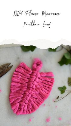 a pink heart shaped object sitting on top of a white surface next to leaves and scissors