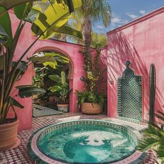 an outdoor hot tub surrounded by potted plants and greenery in front of a pink wall