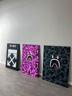 three paintings are displayed on the floor in front of a gray wall with black and purple designs