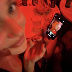 a woman taking a selfie with her cell phone at a table full of bottles and glasses