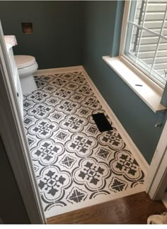 a white toilet sitting next to a window in a bathroom on top of a hard wood floor