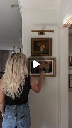 a woman is looking at pictures on the wall in her kitchen and then pointing to them