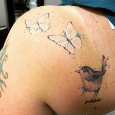 the back of a woman's shoulder with butterflies on it and a bird in flight