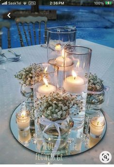 a table topped with lots of candles and vases filled with flowers next to a pool