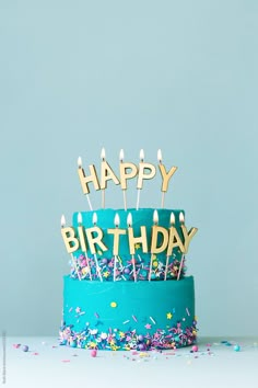 a blue birthday cake with candles and confetti on it that says happy birthday