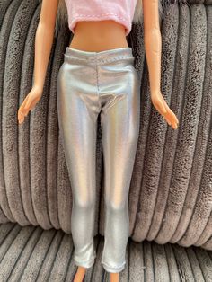 a doll is wearing shiny silver pants and a pink tank top, standing on a couch