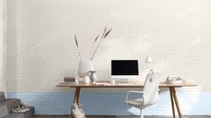 a desk with a computer on it in front of a white brick wall and stairs