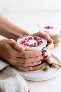 two hands holding a bowl of tea latte with pink flowers on the side and text overlay that reads rose & black tea latte