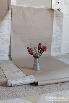 a vase with flowers in it sitting on the floor next to a sheet of paper