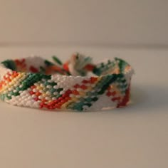 a white bracelet with multicolored beads on it sitting on a table next to a wall