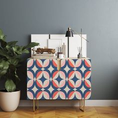 a sideboard with an abstract design on it next to a potted plant