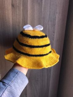 a child's hand wearing a yellow knitted hat with black stripes and a bee on it