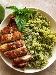 a white plate topped with pasta and meat covered in pesto next to an avocado