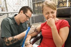 a man and woman sitting next to each other with tattoos on their arms, looking at something