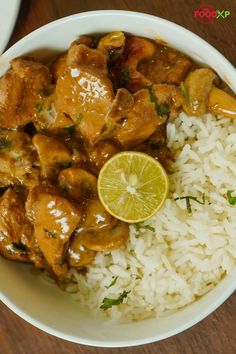 a white bowl filled with rice and chicken next to a slice of lemon on top of it