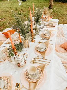 an outdoor table set with plates, silverware and candles