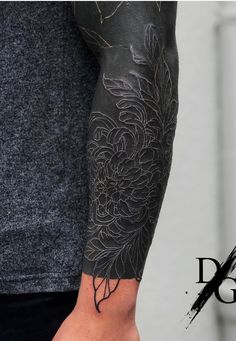 a man's arm covered in black ink with flowers and leaves on the sleeve