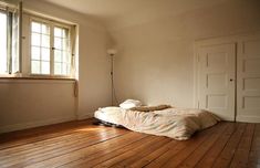 an empty room with wood floors and a bed on the floor in front of a window