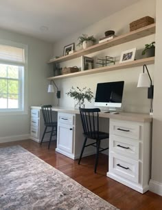 a desk with two chairs and a computer on top of it in front of a window