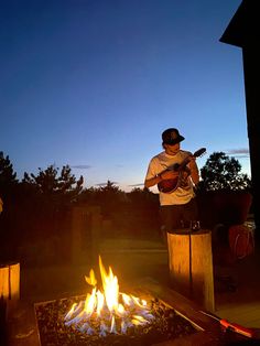 a man playing guitar in front of an open fire pit