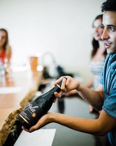 a man is holding a bottle in his hand while two other people are sitting at the bar behind him