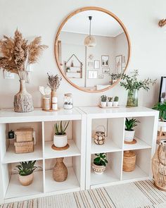 a white shelf with plants and potted plants on it in front of a round mirror