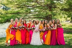 a group of women standing next to each other in front of a lake wearing different colored dresses